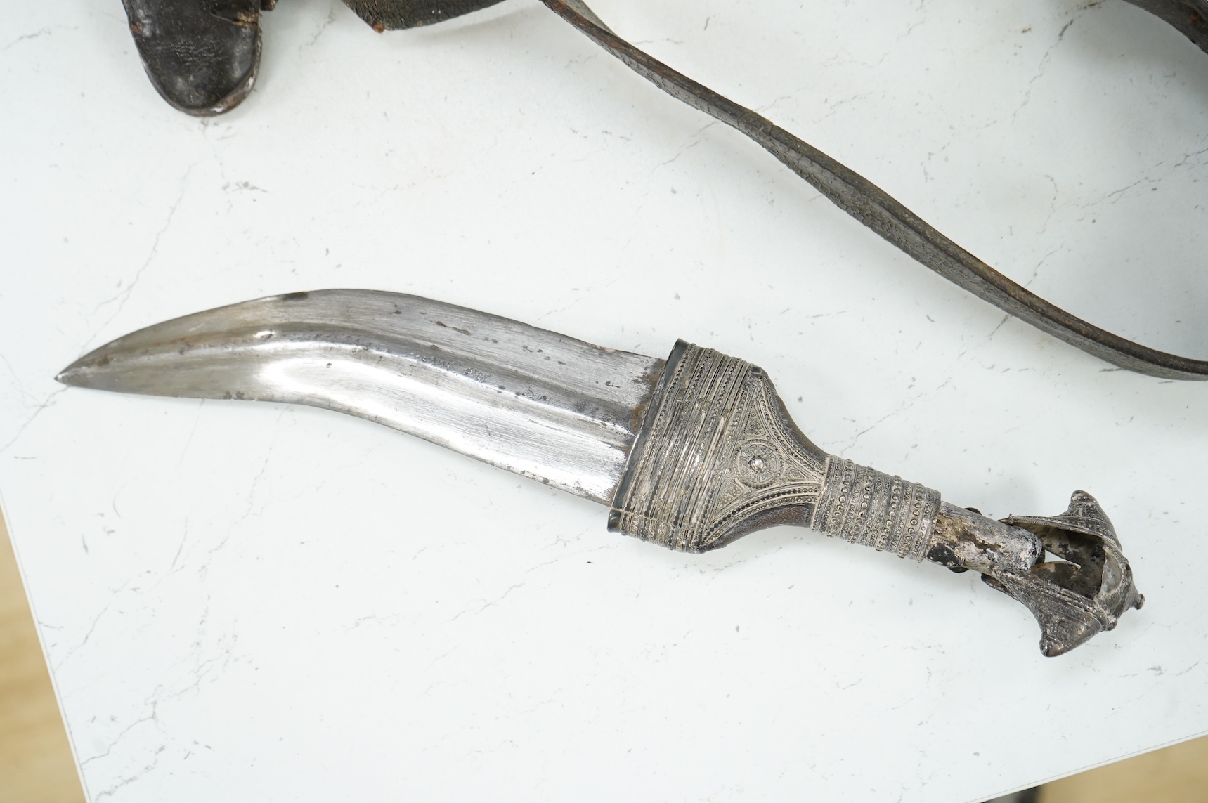 A late 19th century Arab silver mounted dagger jambya with silver filigree mounts to hilt and sheath, in its leather covered scabbard with parts of the original belt